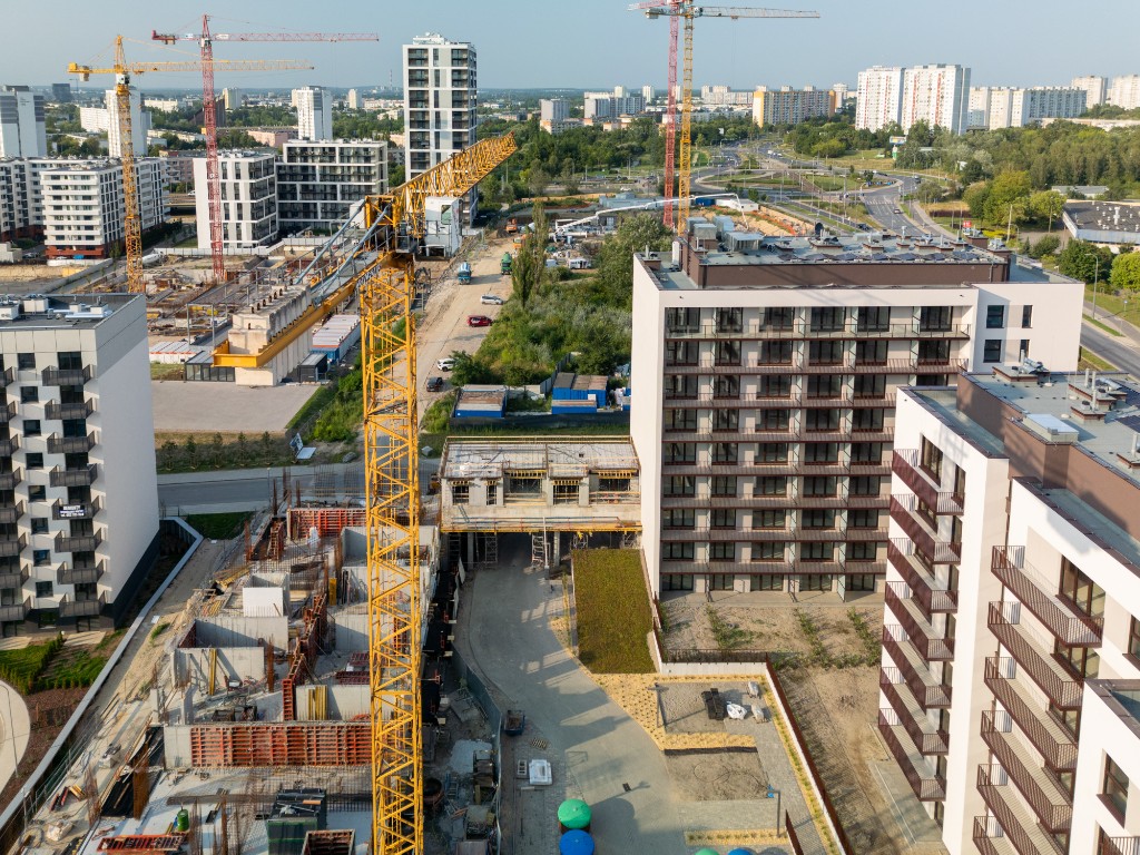 Plac budowy z żurawiem wieżowym i budynkami mieszkalnymi w realizacji, widok z drona